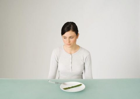 PROD-Young-woman-sitting-in-front-of-plate-with-single-asparagus-looking-away